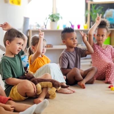 group-small-nursery-school-children-sitting-floor-indoors-classroom-raising-hands_11zon